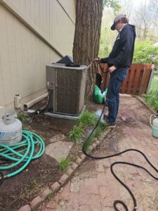 A technician from Apollo Heating and Air cleaning an outdoor air conditioning unit in Bellevue, NE.