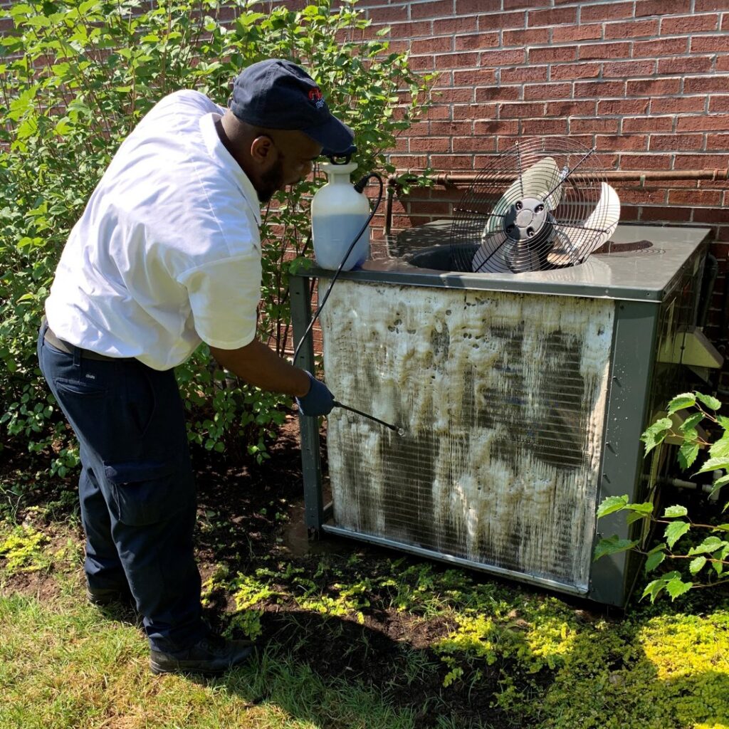 A technician cleaning an outdoor air conditioning unit for Pipe Wrench Plumbing, Heating & Cooling, Inc in Knoxville, TN.