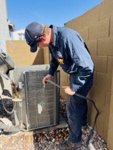 A technician from Rusty's Air Conditioning And Heating cleaning an outdoor AC condenser unit with a hose in Mesa, AZ.