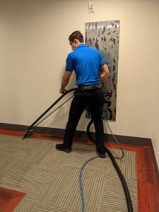 A technician from North Seattle Carpet Cleaning cleaning a patterned office carpet with a wand in Seattle, WA