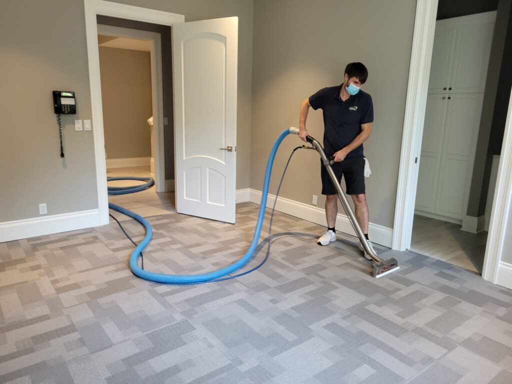 A masked technician cleaning a patterned carpet with professional equipment for Pacific Steam Carpet Cleaning in Gresham, OR.