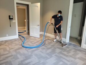 A masked technician cleaning a patterned carpet with professional equipment for Pacific Steam Carpet Cleaning in Gresham, OR.