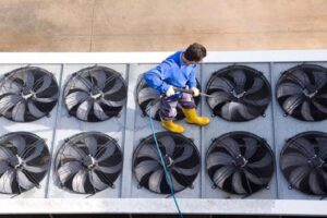 A technician cleaning a large rooftop HVAC unit with multiple condenser fans for Mid-City HVAC, INC. in Chicago, IL.