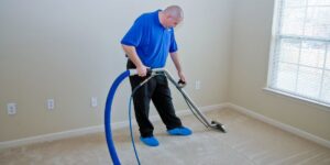 A technician in blue shirt and shoe covers cleaning a room's carpet at J L Williard Carpet Care in High Point, NC.
