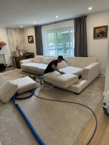 A technician professionally cleaning a large sectional sofa at a client's home by 5 Alarm Carpet Care in West Allis, WI.