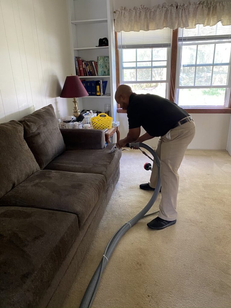 A technician performing upholstery cleaning on a sofa for Rent A Vet Carpet Cleaning in St. Charles, MO.
