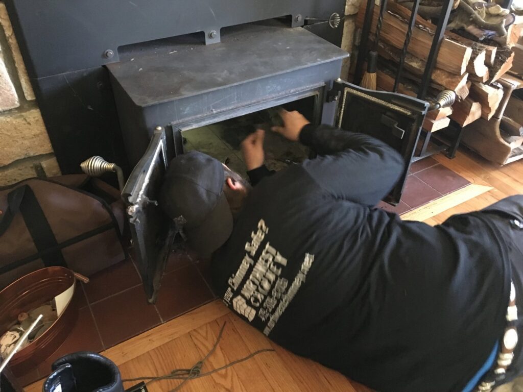 A Northwest Chimney technician cleaning the interior of a wood stove in Bremerton, WA.