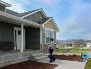 A Prompt Pest Solutions technician clearing spider webs from house eaves with a long pole in Pocatello, ID.