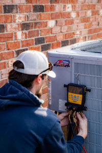 An Allegiance Heating & Air technician connecting HVAC gauges to an outdoor AC unit in Greenville, IN.