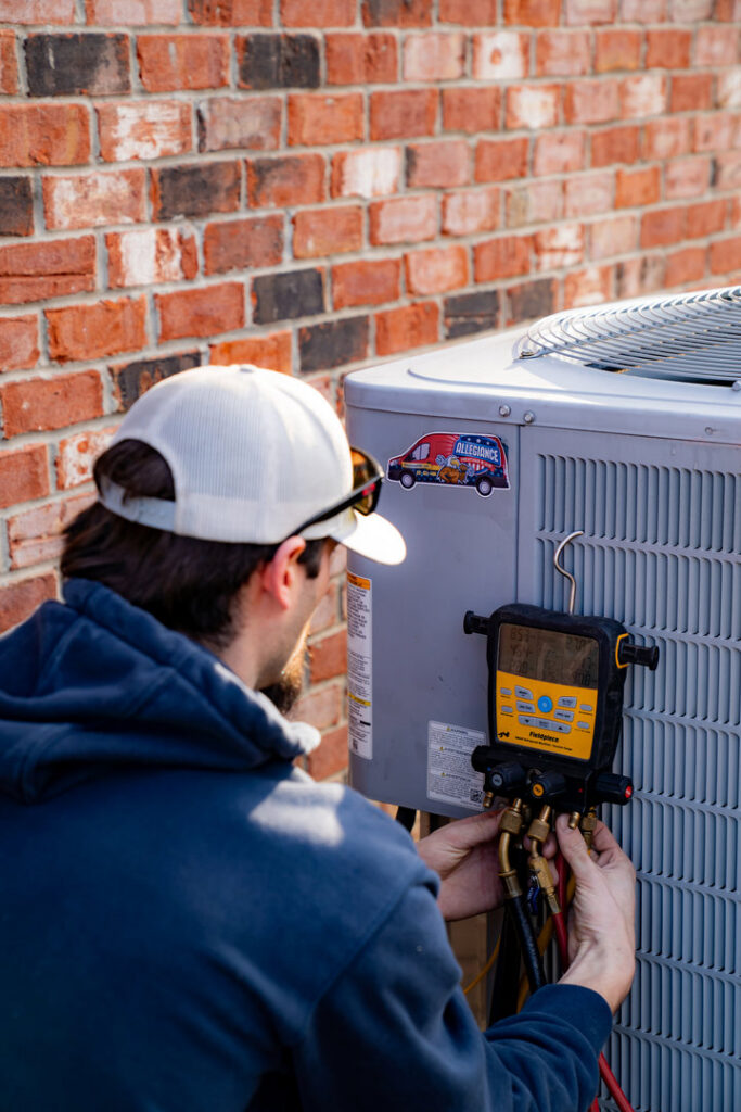 An Allegiance Heating & Air technician connecting HVAC gauges to an outdoor AC unit in Greenville, IN.