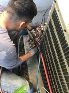 A Hicken Air technician connecting refrigerant lines to an outdoor HVAC condenser unit in Gilbert, AZ