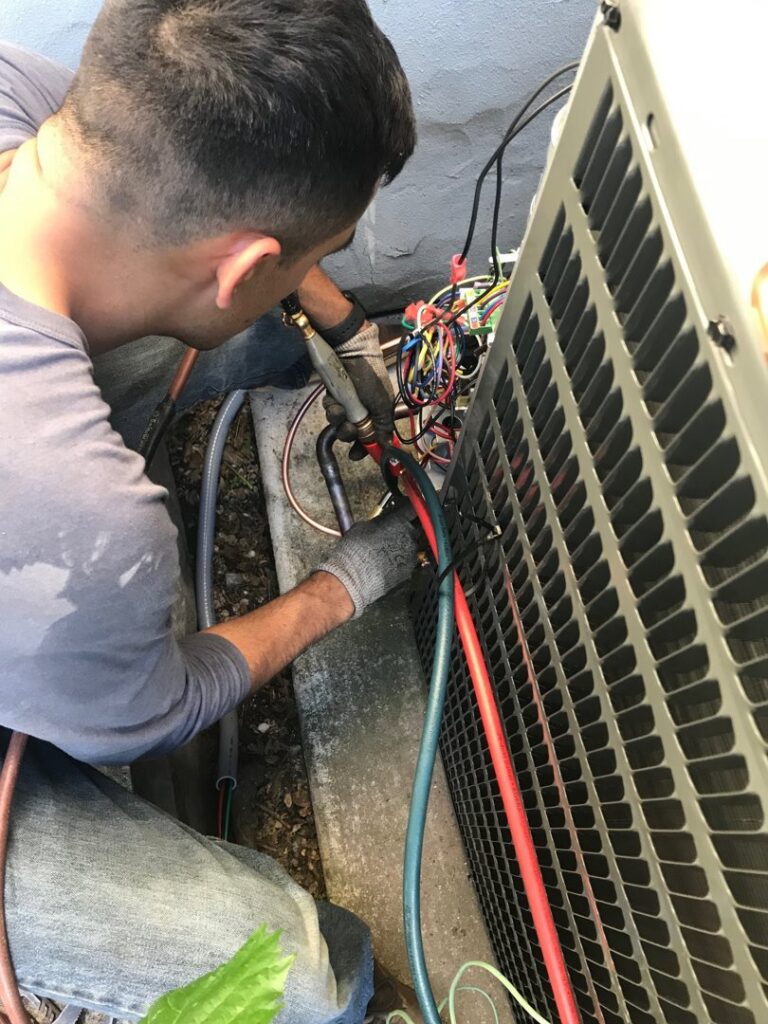 A Hicken Air technician connecting refrigerant lines to an outdoor HVAC condenser unit in Gilbert, AZ