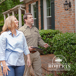 A pest control technician discussing service options with a customer outdoors for Roberts Termite & Pest Control in Austin, TX