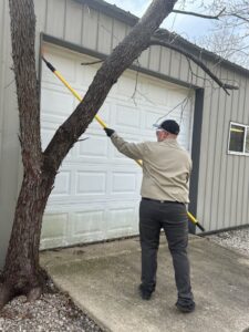 A Diamond Pest Solutions technician in Conway, AR, de-webbing a garage door with a long pole as part of pest control services.