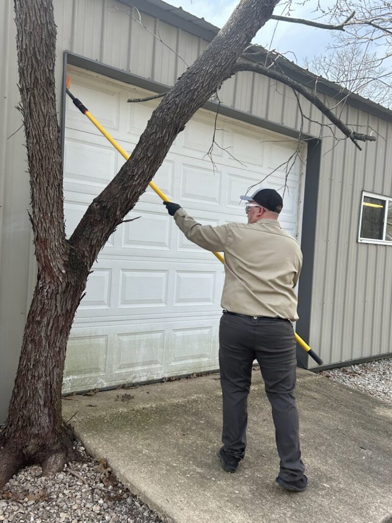 A Diamond Pest Solutions technician in Conway, AR, de-webbing a garage door with a long pole as part of pest control services.