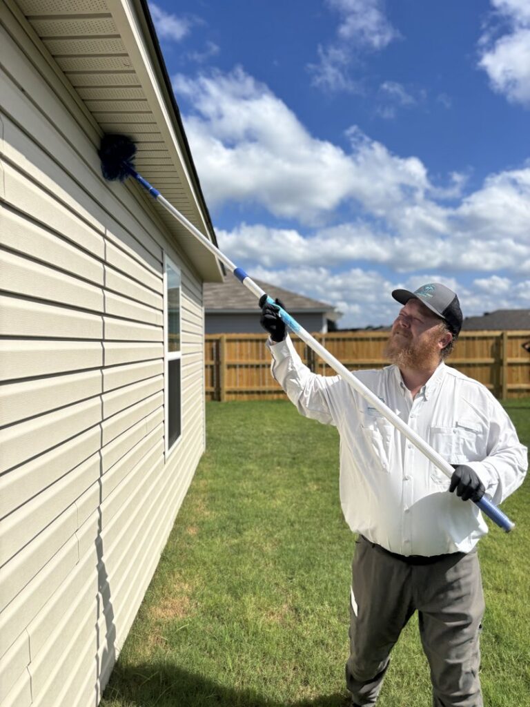 A Diamond Pest Solutions technician in Conway, AR, de-webbing the eaves of a house with a long pole, providing pest control service.