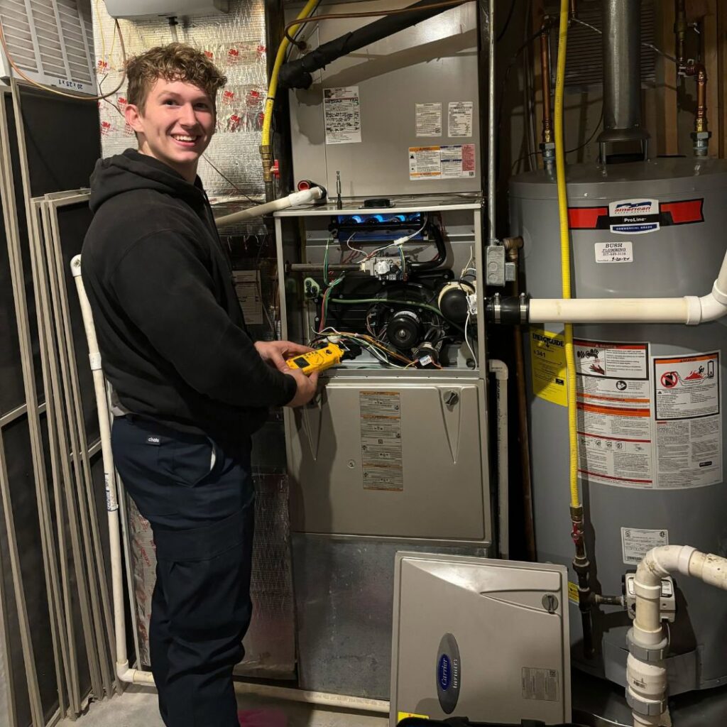 A smiling technician from STAR Heating Cooling Plumbing diagnosing a furnace with a multimeter in Fishers, IN.