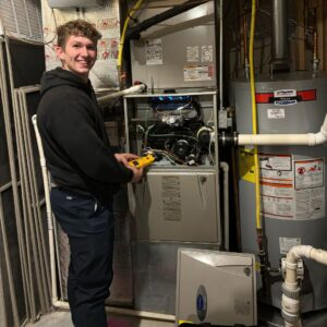 A smiling technician from STAR Heating Cooling Plumbing diagnosing a furnace with a multimeter in Fishers, IN.