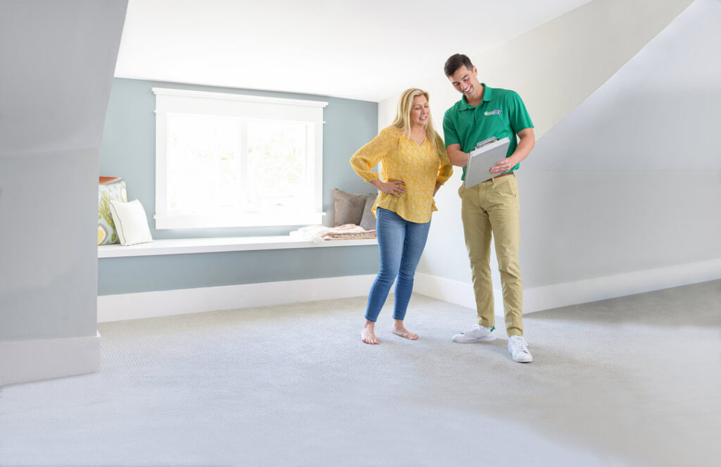 A Brimley's White Glove Chem-Dry technician discusses service details with a client in a carpeted room in Mesa, AZ.