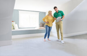 A Brimley's White Glove Chem-Dry technician discusses service details with a client in a carpeted room in Mesa, AZ.