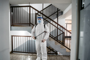 A technician in a protective suit and face shield with a sprayer in a building stairwell by Central Iowa Pest Control Services Inc in West Des Moines, IA