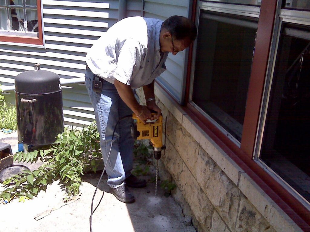 A pest control technician drilling into a house foundation for treatment by All Seasons Pest Control LLC in Topeka, KS.