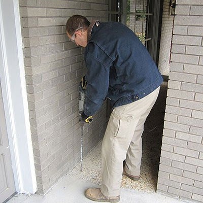 A technician drilling into a house foundation for termite treatment by Curry's Termite, Pest & Animal Control in Little Rock, AR