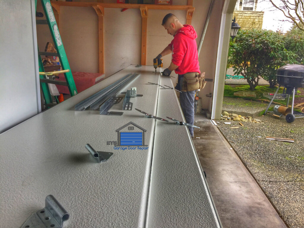 A technician from ETS - Garage Door & Electric Gate Repair Of Bellevue, WA, drilling a garage door panel during a repair.