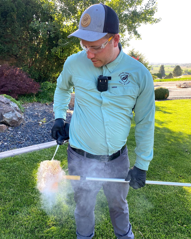 A Nature Shield Pest & Lawn technician dusting for pests in a residential yard in Meridian, ID.