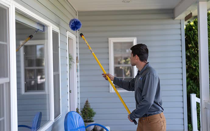 A pest control technician using a duster on a long pole to treat a porch ceiling for Pest Control Consultants in Sycamore, IL.