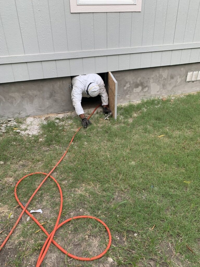 A D' Bug Man Pest Control technician entering a crawl space under a house for pest or wildlife control in Arlington, TX.