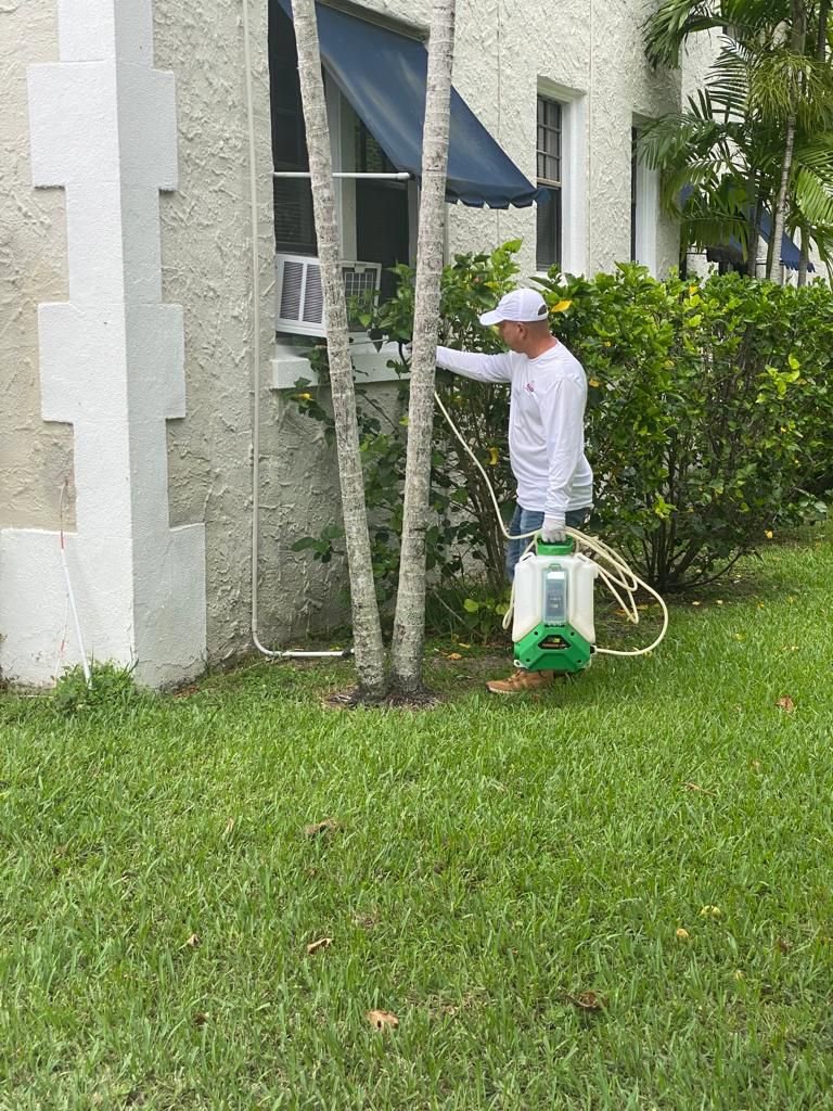 A technician performing exterior pest spraying with a backpack sprayer for PNP Pest Solutions LLC in Miami, FL.