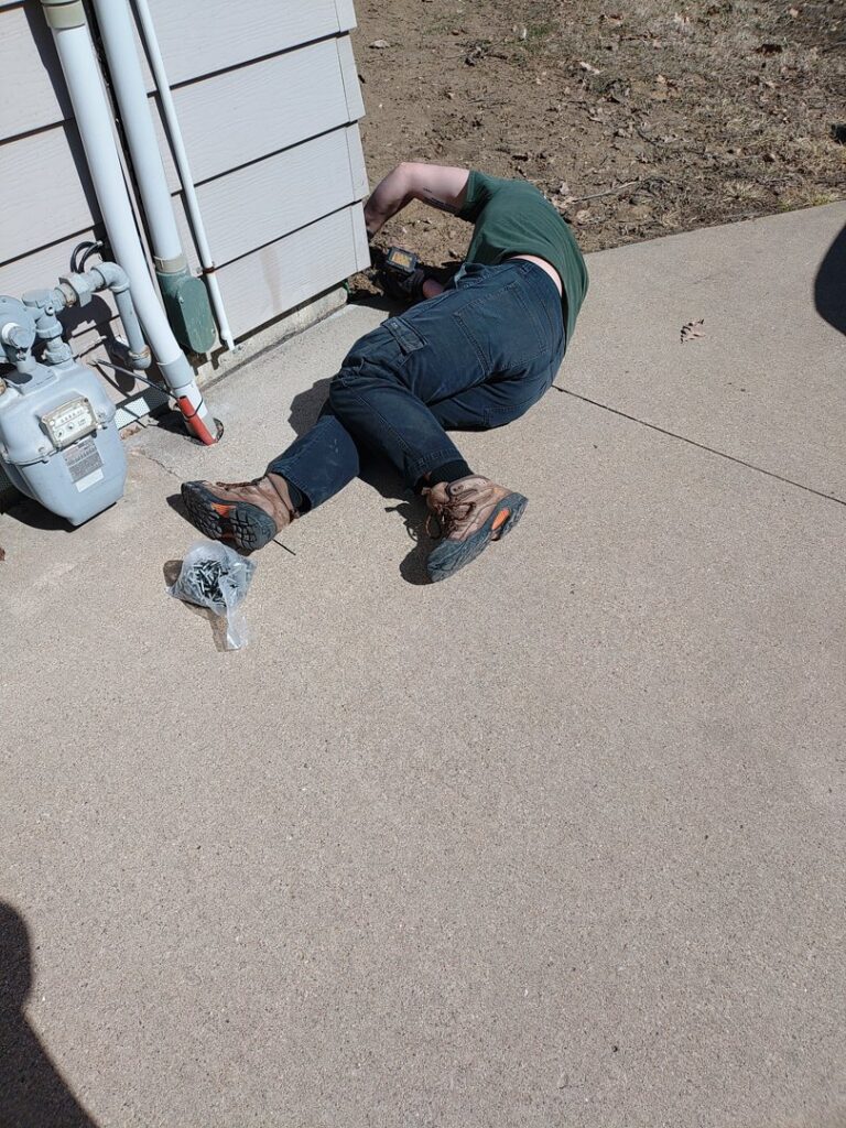 A pest control technician performing an exterior treatment or sealing work on a house for Enviro-Pest Solutions in Waterloo, IA.