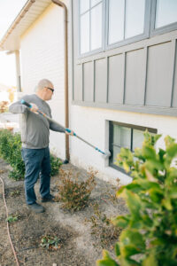 A technician performing exterior pest treatment on a house wall and window for Thrive Pest Management in Sandy, UT