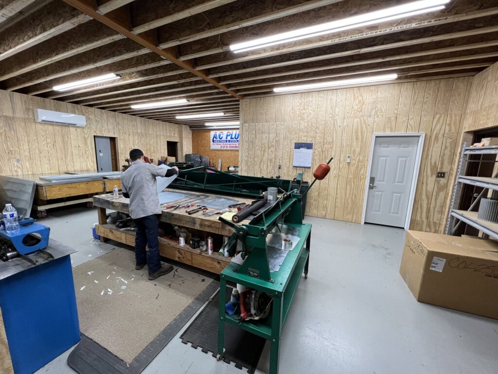 A technician fabricating metal ductwork in a workshop, with a mini-split unit visible, for A/C Company Since 1988 in Murfreesboro, TN.
