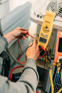 Close-up of a technician's hands diagnosing an outdoor AC unit with a multimeter for Ridgeline Heating and Cooling in Idaho Falls, ID.