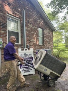 A Milan Heating & Air technician hauling an old outdoor HVAC unit away from a residence in Milan, TN.