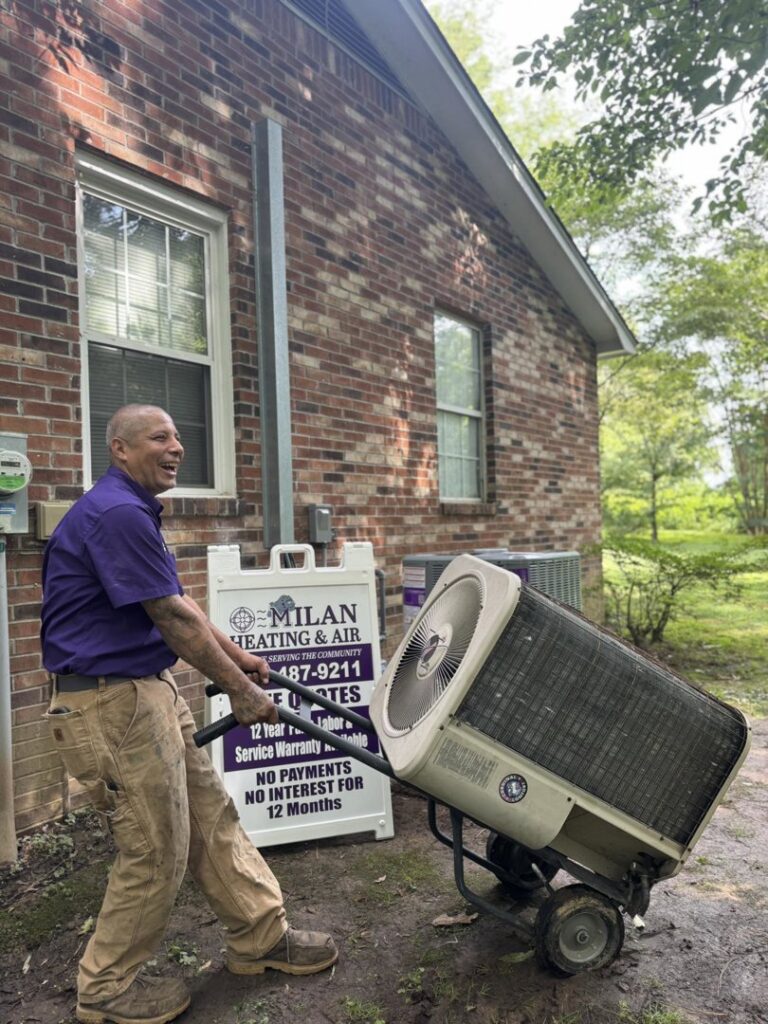A Milan Heating & Air technician hauling an old outdoor HVAC unit away from a residence in Milan, TN.