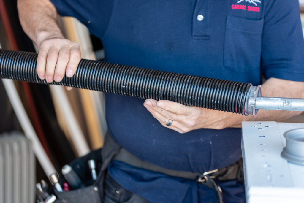 A garage door technician holding a new torsion spring, ready for installation or repair by Above The Rest Garage Door in Colorado Springs, CO.