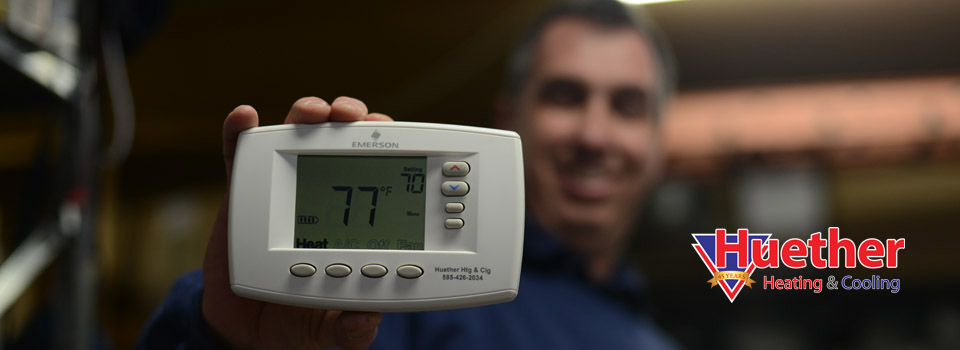 A Huether Heating & Cooling Inc technician holding a digital thermostat in Rochester, NY.