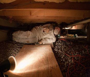 A technician in protective gear inspecting a dark crawl space for Eliminex Pest Control Wildlife & Attic Cleanup in East Brunswick, NJ.
