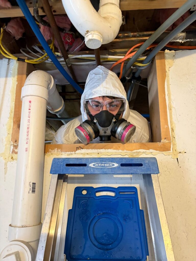 A technician in a hazmat suit and respirator inspecting a crawl space for Profishant, inc. in New Bedford, MA.