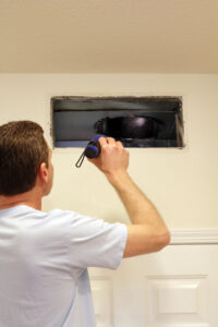 A technician using a flashlight to inspect an air duct through an open wall vent by Wright Way Air Duct Cleaning in Streamwood, IL