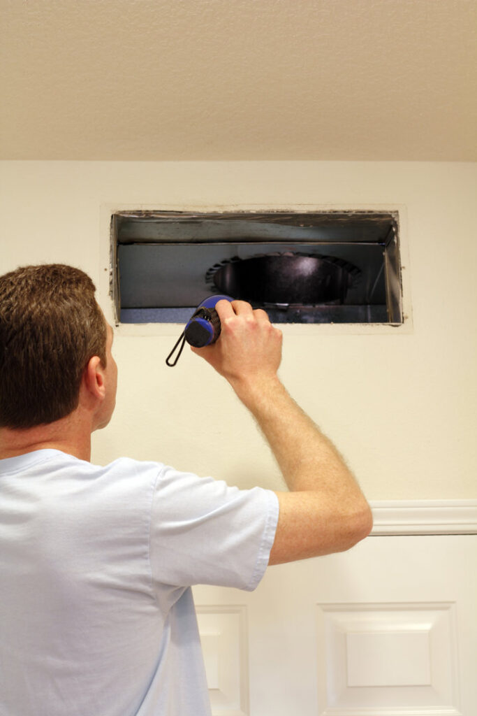 A technician using a flashlight to inspect an air duct through an open wall vent by Wright Way Air Duct Cleaning in Streamwood, IL