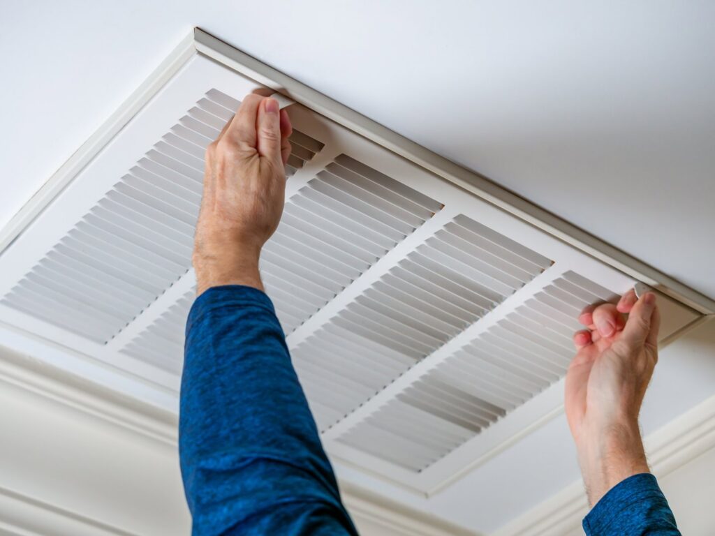 A technician inspecting or cleaning an air return vent on a ceiling for Precision Vac in Thornton, CO.