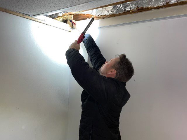 A PestNation technician inspecting an attic space with a flashlight for pests or wildlife in Buford, GA