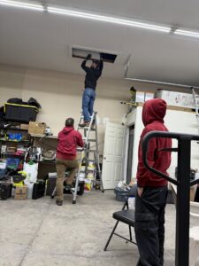 A pest control technician on a ladder inspecting an attic opening, performing work for Tailor Made Pest and Wildlife in Louisville, KY.