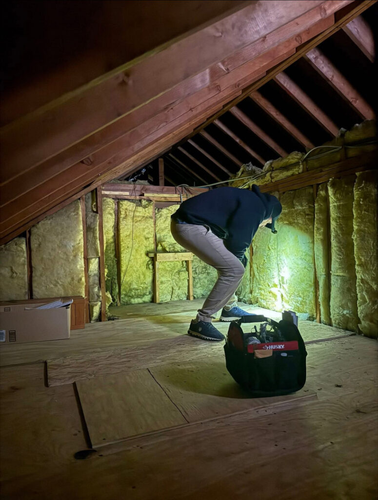 A pest control technician inspecting an attic with a flashlight for signs of pests at Devlins Pest Control in Reading, PA.