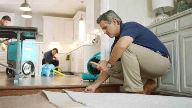 A technician inspecting lifted carpet with a moisture meter during restoration by Xtreme Clean Restoration & Carpet Care in San Antonio, TX