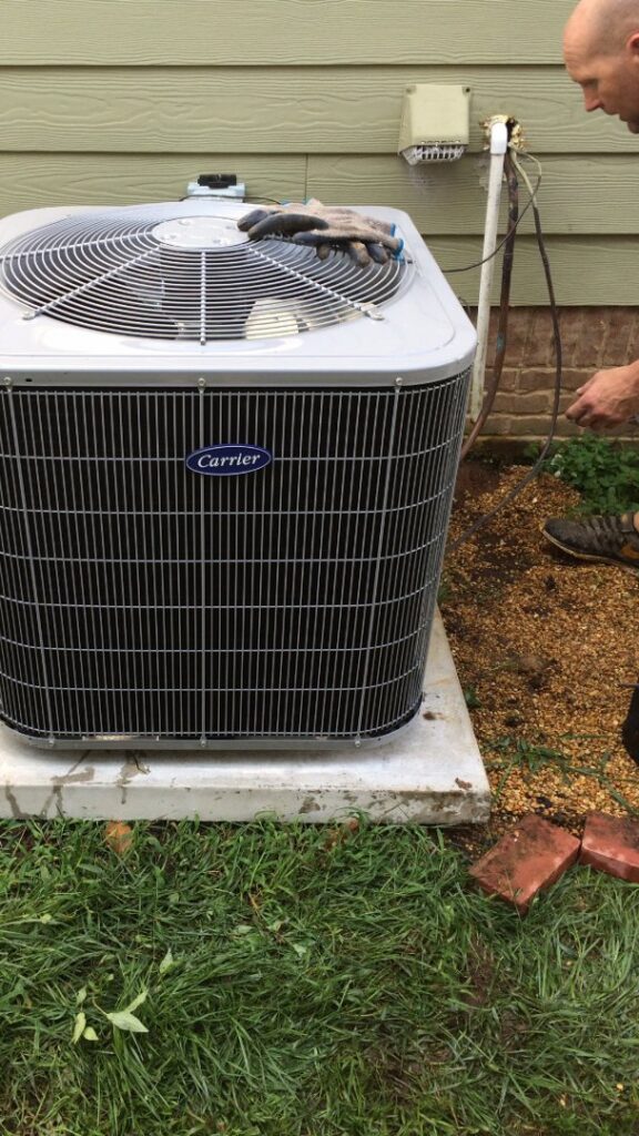 A technician inspecting a Carrier outdoor AC unit for Malone Heat & Air, Inc. in Chattanooga, TN